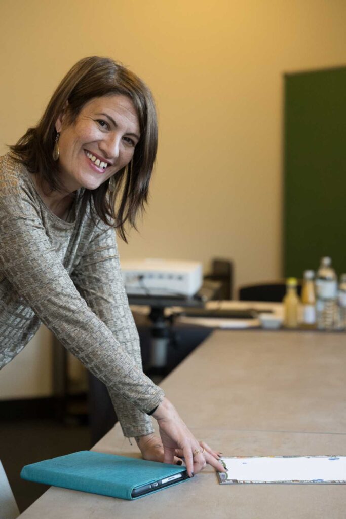 Vivien Schulter lehnt sich lächelnd über einen Besprechungstisch und bereitet Unterlagen für einen Change-Workshop vor.