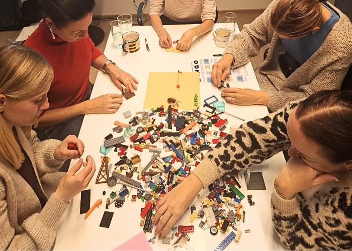Mehrere Erwachsene arbeiten gemeinsam mit bunten LEGO-Steinen an einem Tisch während eines Workshops, konzentrierte Teamarbeit und Austausch.