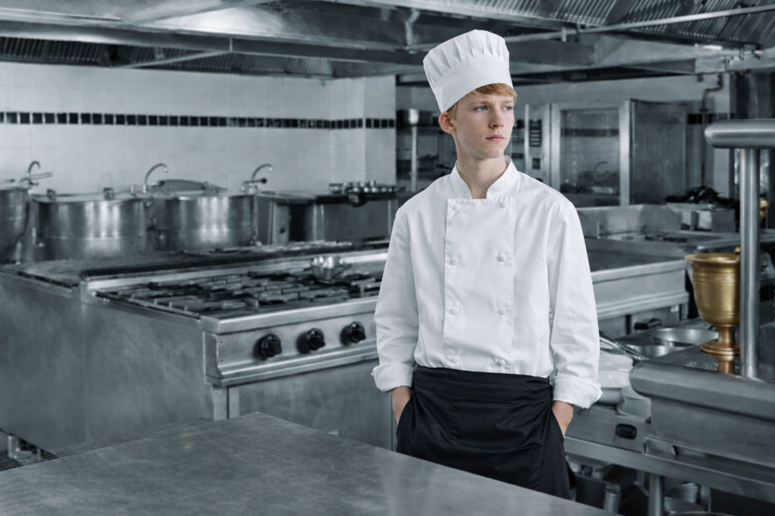 Junger Kochlehrling steht alleine in einer professionellen Hotelküche im Tourismus
